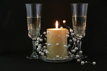 Two glasses of champagne, a red candle, a wreath on a white background.