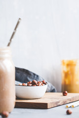View at a part of a breakfast table with smoothie, peanut butter and hazelnuts. Copy space, white background, lifestyle photo
