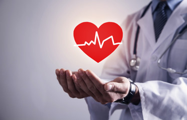 Doctor standing with stethoscope holding red heart with heartbeat.