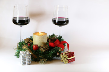 Two glasses of red wine, a golden candle, a wreath on a white background.