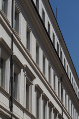 Large white stone building in Rome, Italy, with rows of windows in parallel lines against a blue sky