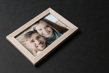Photo of happy couple in frame with cracked glass on dark background. Concept of divorce