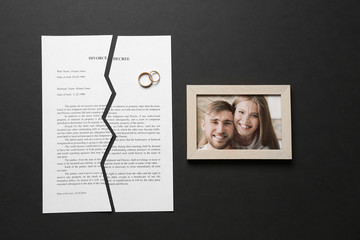 Fototapeta na wymiar Torn divorce decree, rings and broken frame with photo on dark background