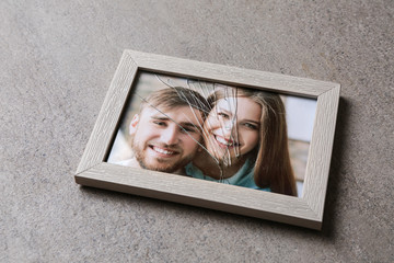Photo of happy couple in frame with cracked glass on table. Concept of divorce