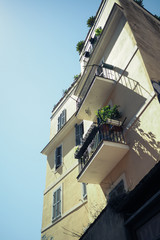 Fototapeta na wymiar Pale yellow building with metal juliet balconies and garden boxes against a blue sky, in Rome, Italy