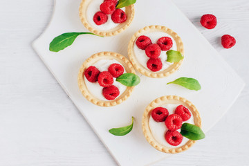 Tartlets with cream and raspberry on a white wooden board