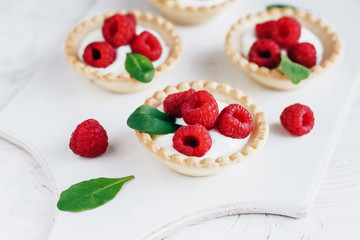 Tartlets with cream and raspberry on a white wooden board