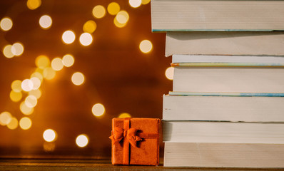 Christmas gift box and pile of books with fairy lights on background