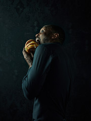 The young african american man eating hamburger and looking away on black studio background