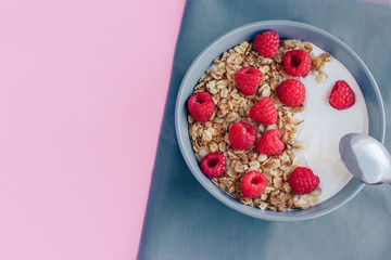 Healthy Breakfast yogurt with granola and raspberry on pink gray background top view copy space