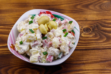 Potato salad with marinated mushrooms, sausage, onion and mayonnaise on wooden table