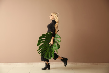 Beautiful woman with green tropical leaf near color wall