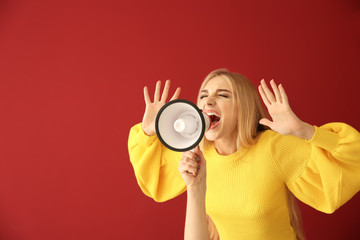 Emotional young woman with megaphone on color background