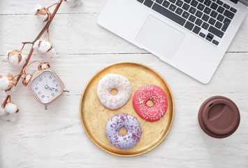 Composition with tasty doughnuts and laptop on white wooden table