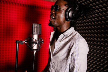 African man with dreadlocks and headphones in the recording Studio singing loudly close-up. Side...