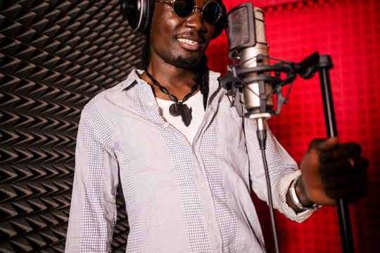 African Man In A Red Recording Studio. The Guy Singer Standing With A Microphone In An Enclosed Space Music Concept