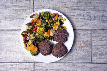 Meat patties with vegetables on a white plate on a gray background