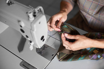 Tailor workplace: view from above of electrical sewing machine and close-up of female hands with needle stitching together garment details before sewing. Handmade exclusive fashionable clothes making.