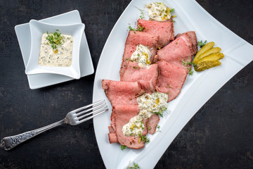 Traditional lunch meat with sliced cold cuts roast beef and remoulade as top view on a white plate on black background