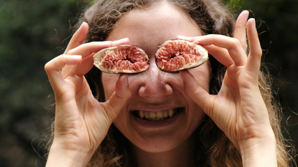 Portrait of woman holding a half of a fig in front of her eyes - teasing and playing