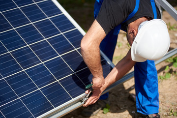 Close-up of technician working on exterior voltaic stand-alone solar panel system installation on bright sunny summer day. Renewable ecological cheap green energy production concept.
