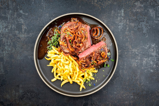 Traditioneller Zwiebelrostbraten aufgeschnitten mit  schw&auml;bische Sp&auml;tzle und R&ouml;stzwiebel als Draufsicht auf einem Modern Style Teller mit brauner Sauce und Textfreiraum