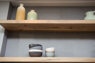 Home decor - various neutral colored vases wooden shelf against grey wall.