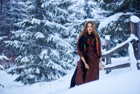 Full length portrait of attractive young slim woman with long straight loose hair in long woolen stylish dress and dark kerchief with bright floral pattern outdoors i on snowy winter day.