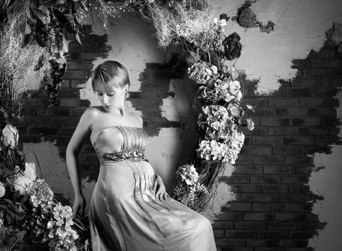 Beautiful pregnant woman in a gown sitting on floral decorative swing