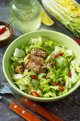 Diet menu, Vegan food. Healthy salad with Chinese cabbage, chicken, sesame and chili pepper on a dark stone table.