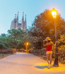 Obraz premium Young woman tourist in front of the famous Sagrada Familia landmark at evening time in Barcelona
