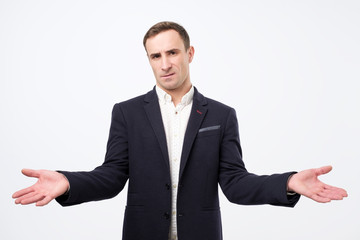 Man isolated on grey background being at a loss, showing helpless gesture with arm and hands