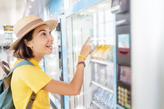Happy asian woman using a modern beverage vending machine to buy drinks