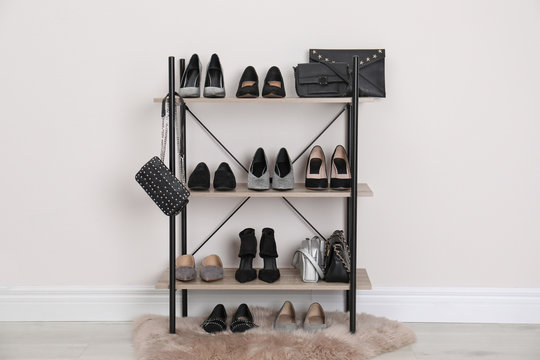 Shelving unit with stylish shoes and purses near white wall. Element of dressing room interior