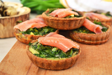 Mini quiche with spinach, scrambled eggs and lightly salted salmon. Delicious appetizer on wooden cut board.