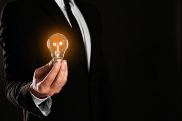 Businessman holding lamp bulb against dark background, closeup. Space for text