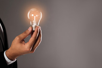 Businessman holding lamp bulb against gray background, closeup. Space for text