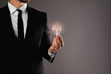Businessman holding lamp bulb against gray background, closeup. Space for text