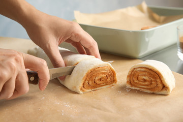 Woman cutting dough for cinnamon rolls on parchment at table, closeup