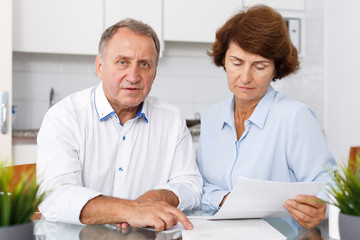 Naklejka na ściany i meble Unhappy mature family couple sitting at kitchen table with documents