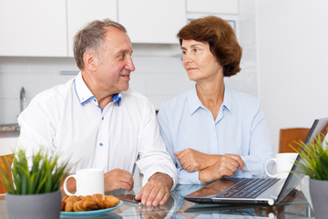 Mature man and woman talking while working at laptop together at home