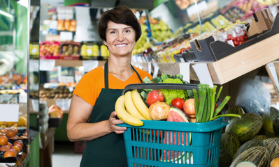 Positive woman seller showing basket with vegetables and fruits