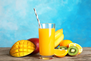 Glass with tasty mango juice and fresh fruits on table against color background