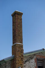 Abandoned ruin of oven chimney. Broken furnace. Snowy roof and blue sky background in the winter