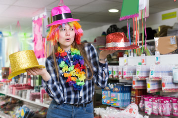 Fototapeta premium Smiling girl looking for party hats in store of festival outfits