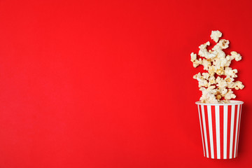 Overturned paper cup with tasty popcorn on color background, top view. Space for text