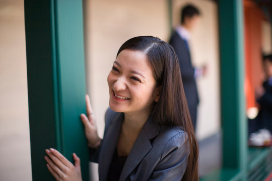 Young adult business woman standing beside a post smiling.