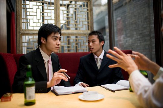 Young adult businessmen sitting at a table in a bar drinking beers and smoking.