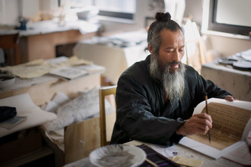 Mature man sitting and painting in a classroom.