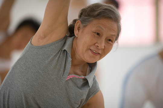 Senior adult woman doing yoga poses with a group of women  in a class.